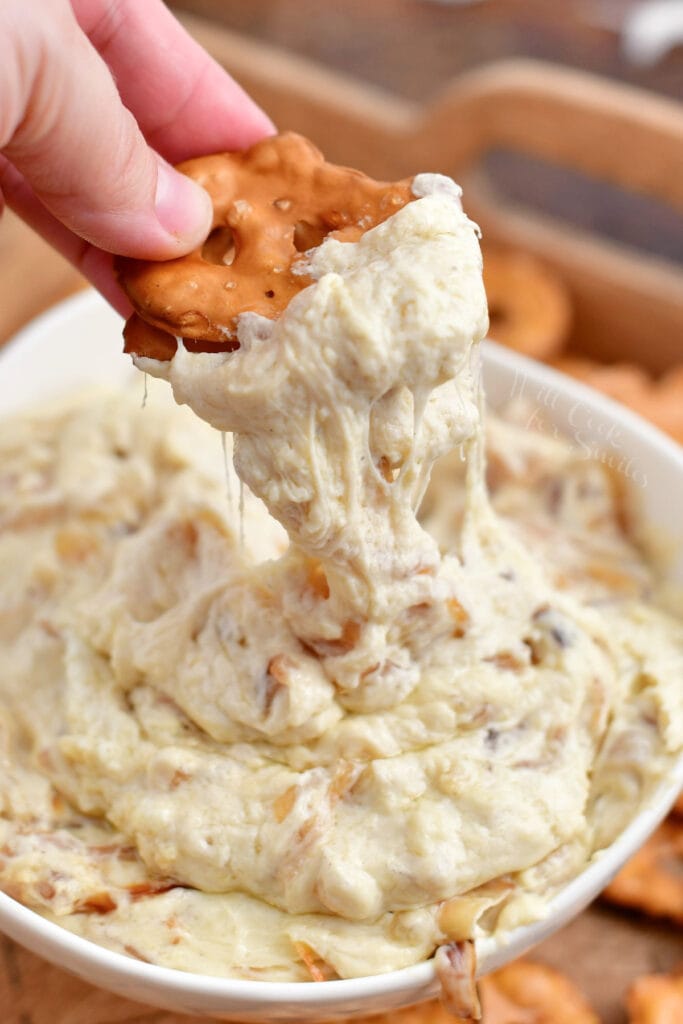 scooping onion dip out of a white bowl with pretzel chips