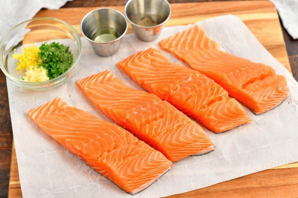 4 fresh salmon fillets on parchment paper with fresh herbs for healthy salmon recipe