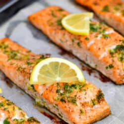 closeup image of oven baked fish topped with fresh herbs and lemon slices