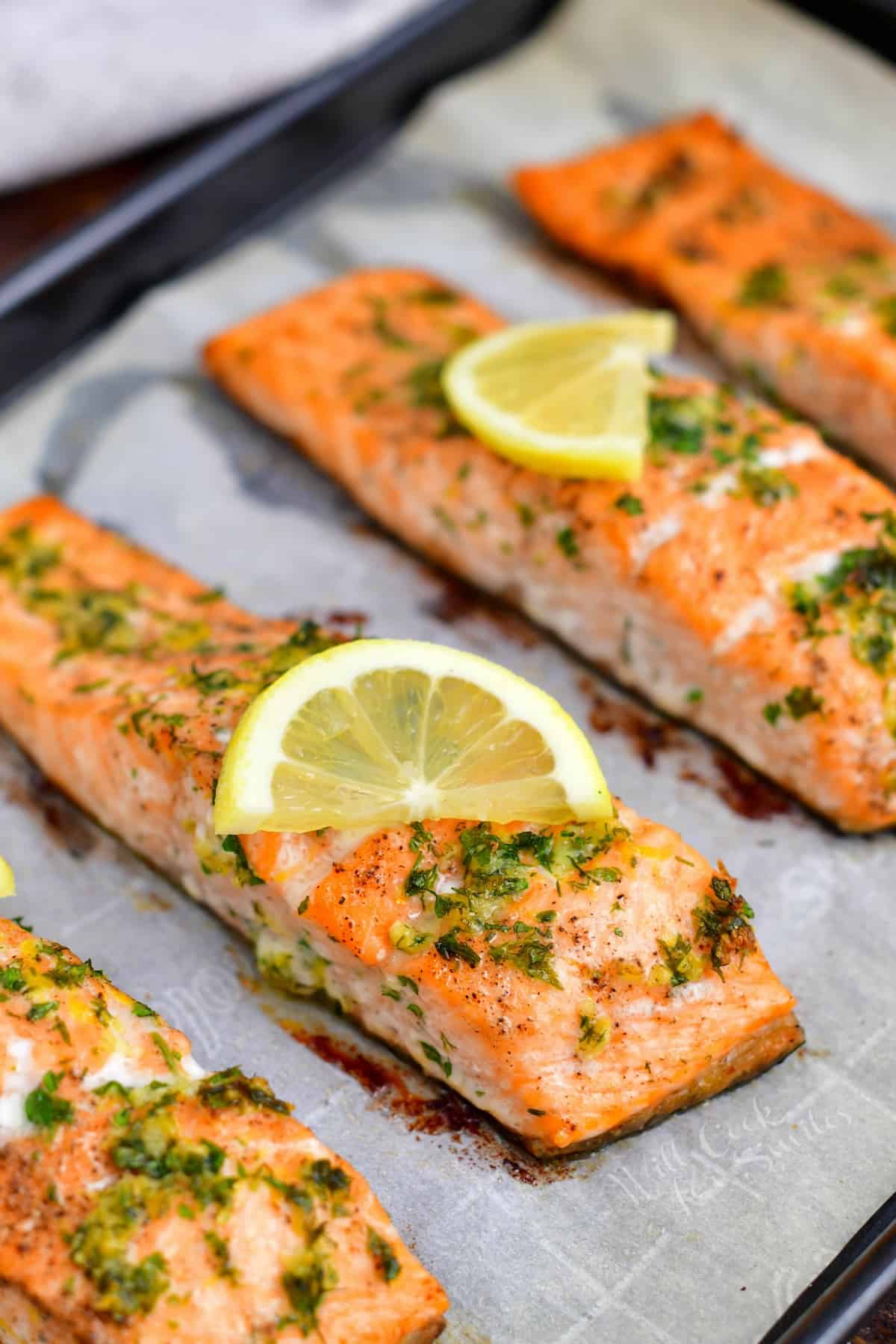 closeup image of oven baked fish topped with fresh herbs and lemon slices