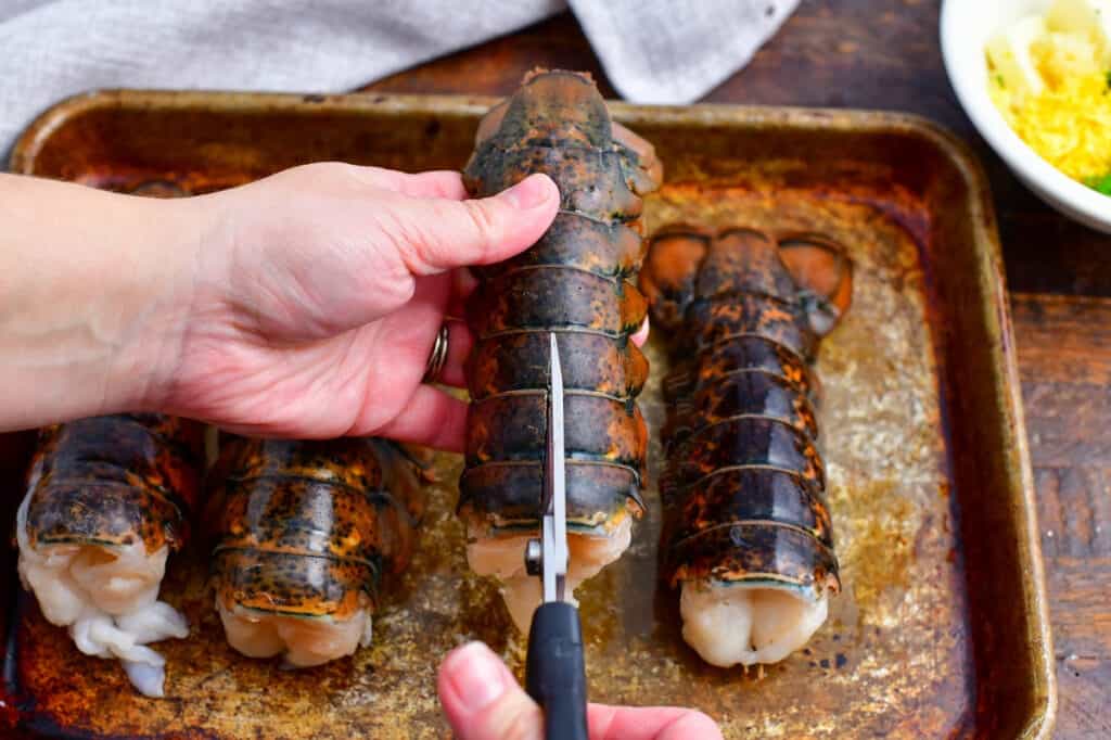 woman's hand holding lobster tail in one hand using scissors to cut the shell open