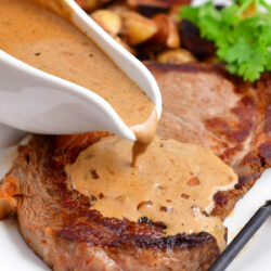 pepper sauce being poured over cooked steak on white platter