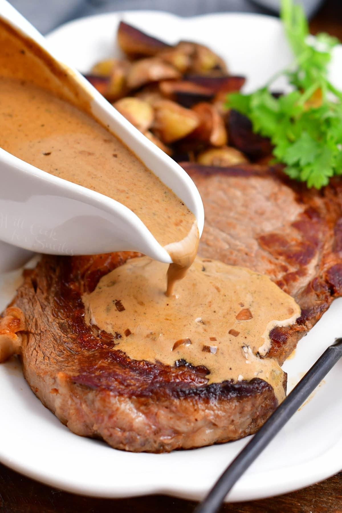 pepper sauce being poured over cooked steak on white platter