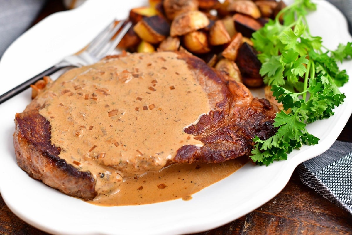 closeup: plate of steak with pepper sauce, crispy roasted potatoes, garnish of parsley