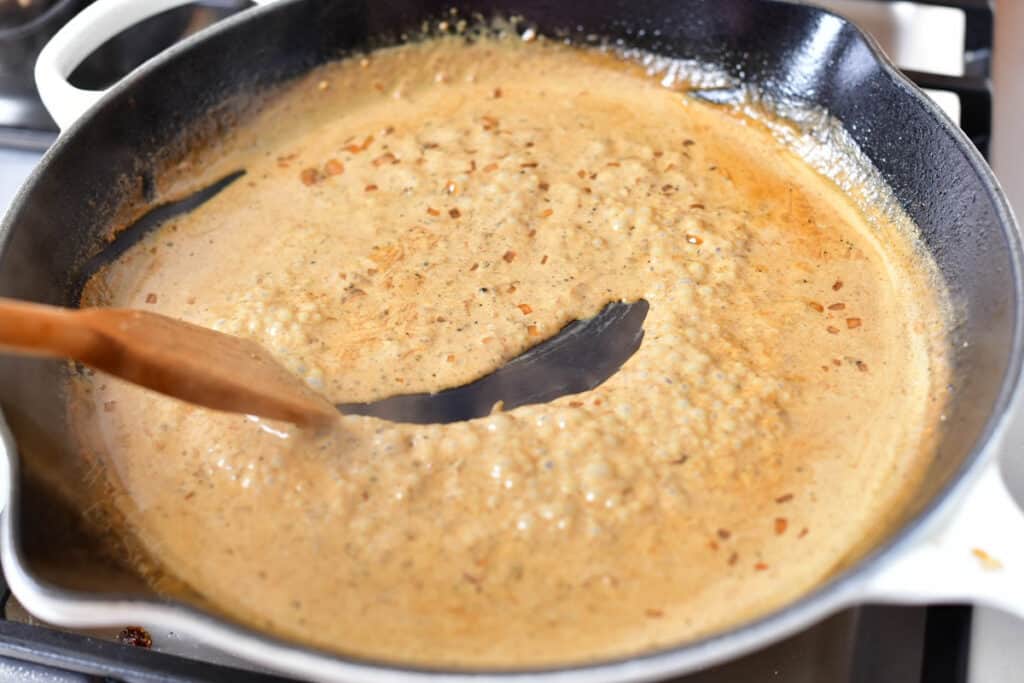 wooden spatula being pulled through thickened peppercorn sauce