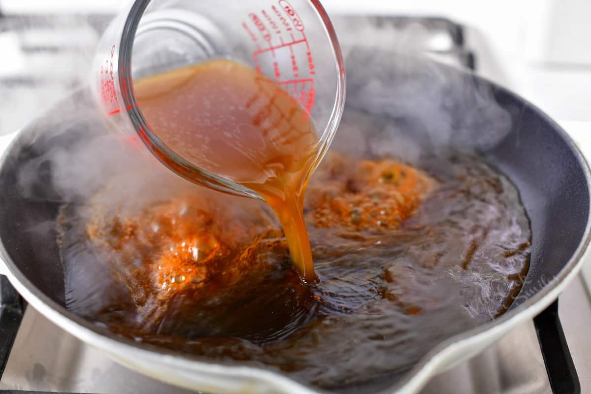 pouring beef stock into skillet to make reduction