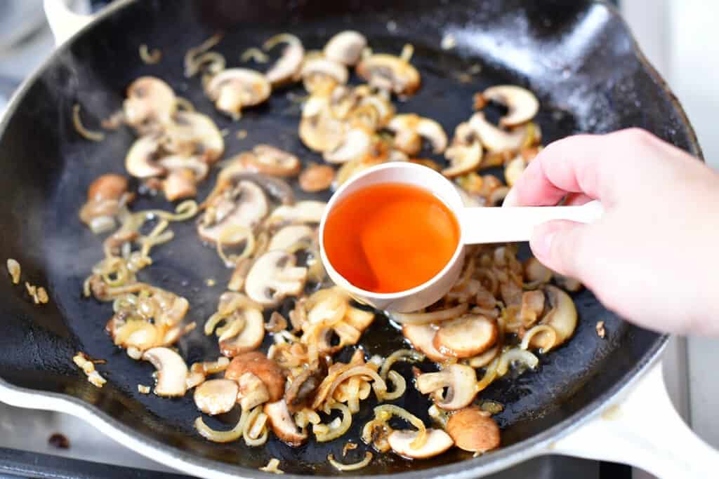 pouring cognac into skillet over sauteed mushrooms and shallot
