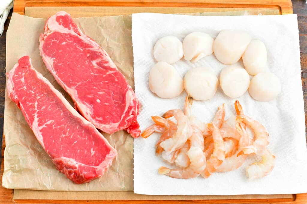 2 raw rib eye steaks, several raw shrimp, and 8 raw scallops