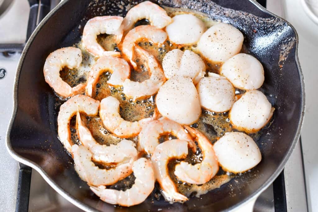 scallops and shrimp being cooked in pan of butter