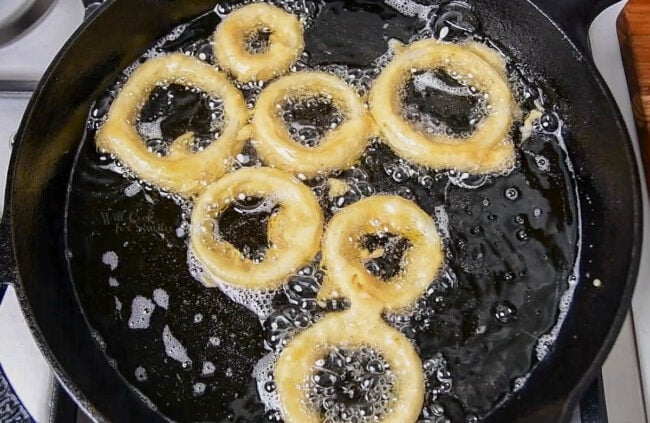 battered onion rings frying in skillet of oil