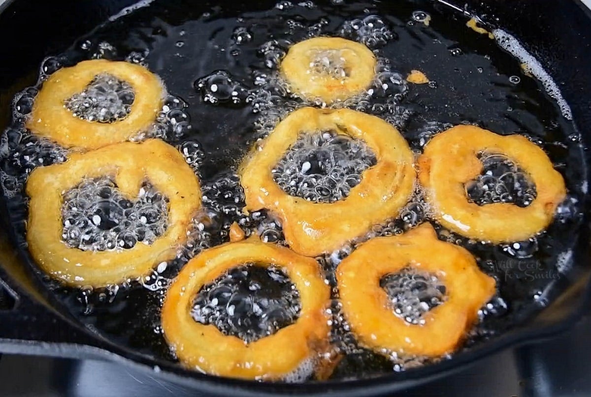 darker color of onion rings frying in skillet of oil