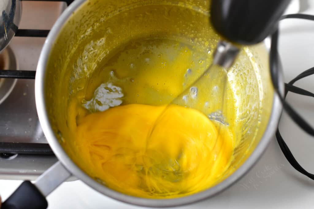 Eggs and butter are being whisked in a large pot.