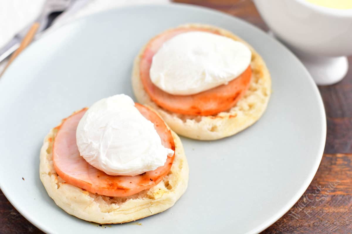 English muffins are on a plate and topped with Canadian bacon and poached eggs.