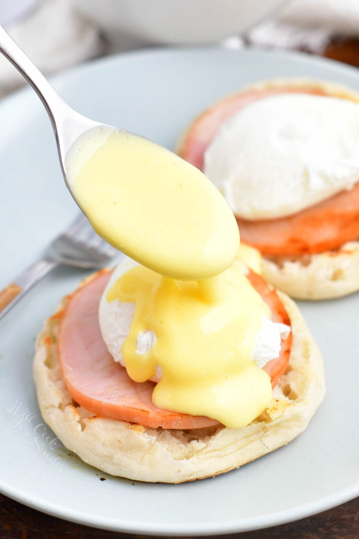 Hollandaise sauce is being drizzled on top of Eggs Benedict.