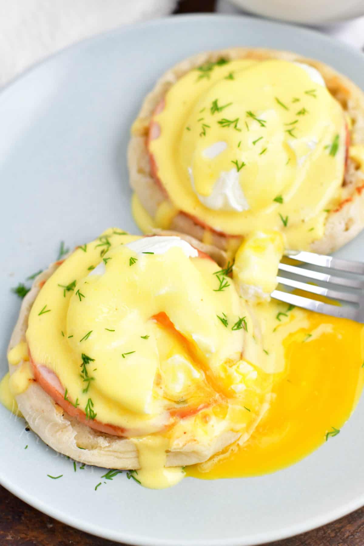 A fork has sliced into a serving of eggs Benedict, causing the yolk to run onto the white plate.