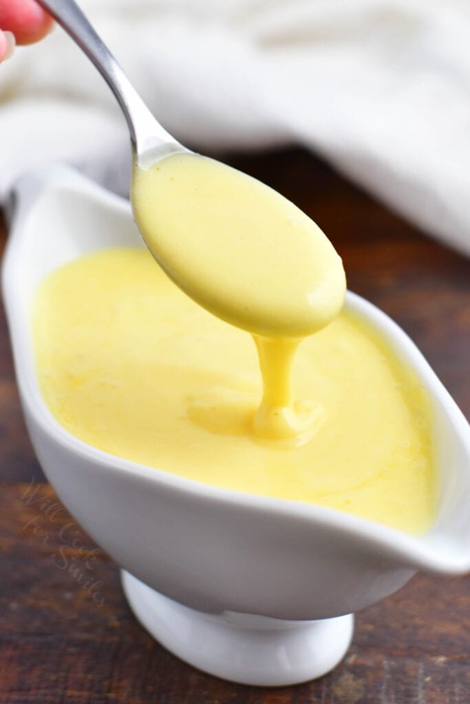 Hollandaise sauce is being drizzled with a spoon over the serving container.
