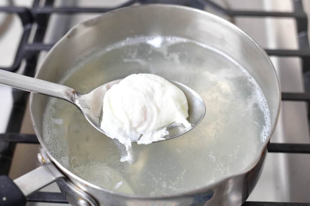 A spoon is lifting a poached egg from the hot pot.