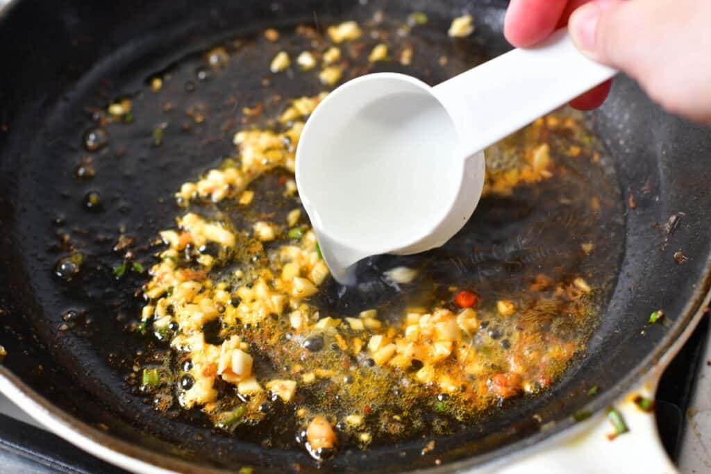 pouring pasta water into skillet of sauteed garlic