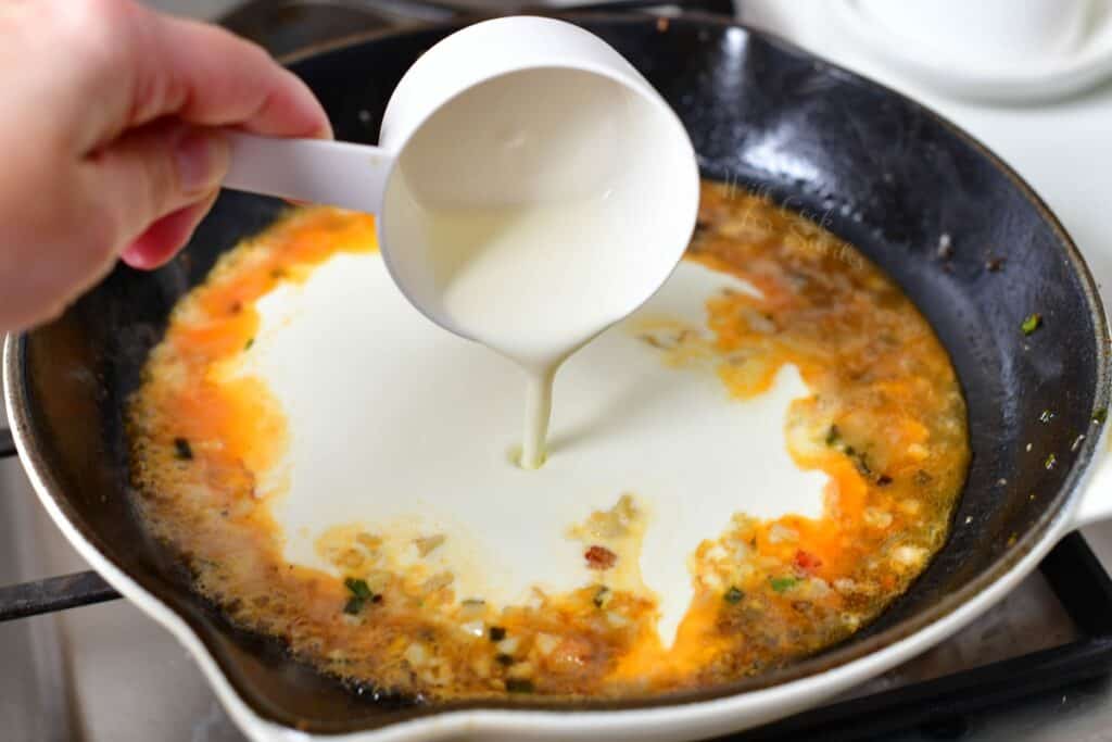 adding heavy cream to saute pan for a seafood pasta sauce