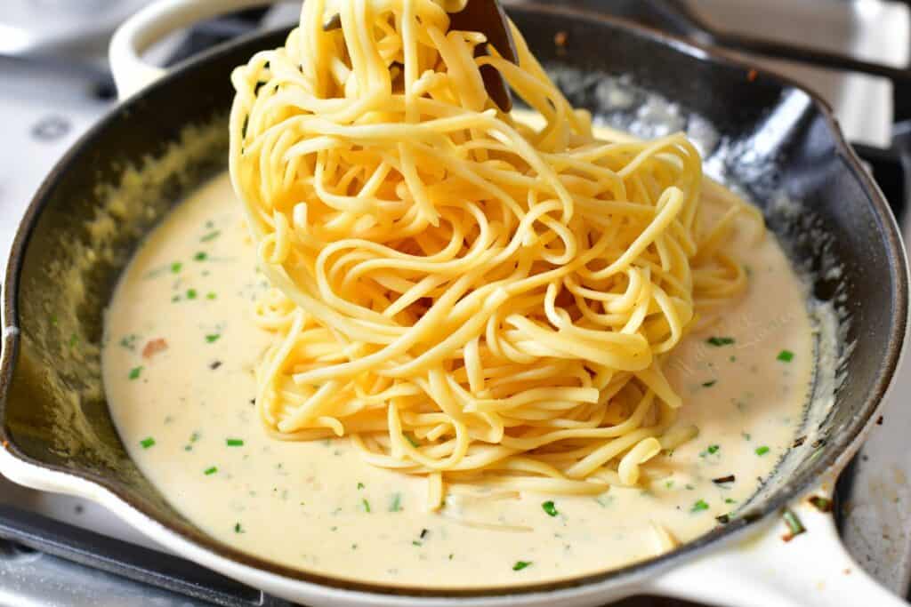 adding cooked linguine to a skillet of creamy sauce