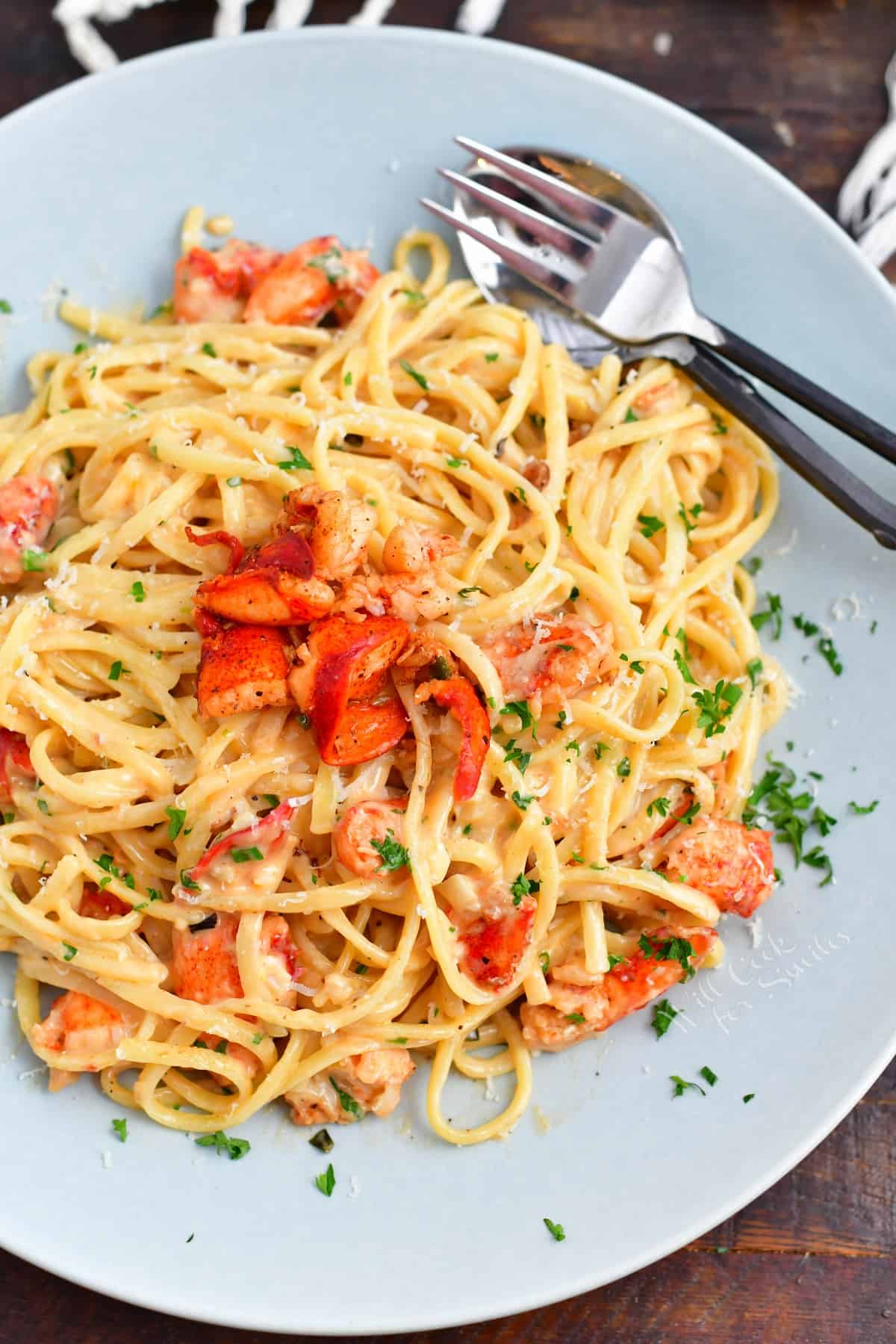 blue plate with creamy spaghetti pasta in the center topped with lobster meat and fork and spoon.