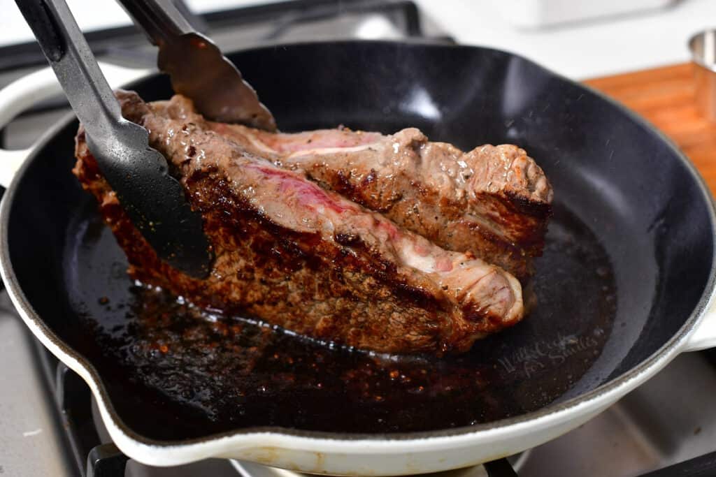 tongs holding beef on its side to render the fat