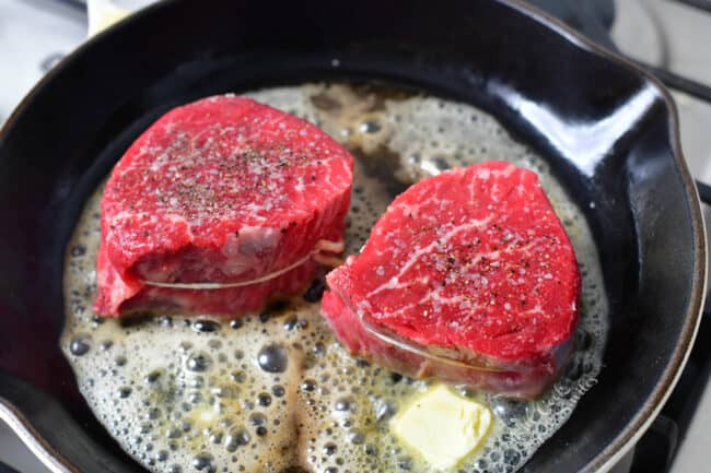 two pieces of steak cooking in a pan