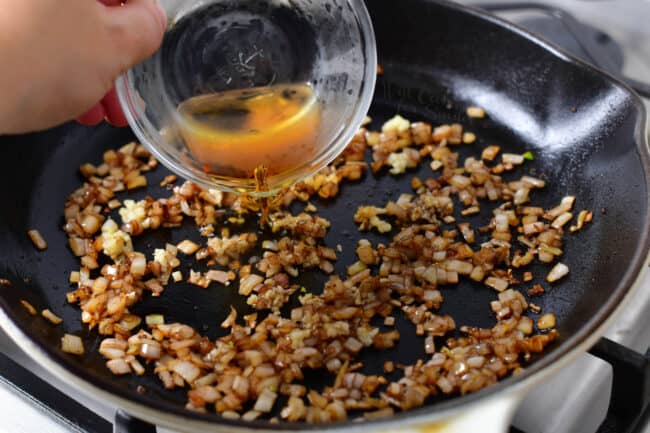 person adding cognac into sauteed shallots and garlic