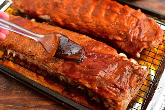 brushing bbq sauce onto two racks of pork