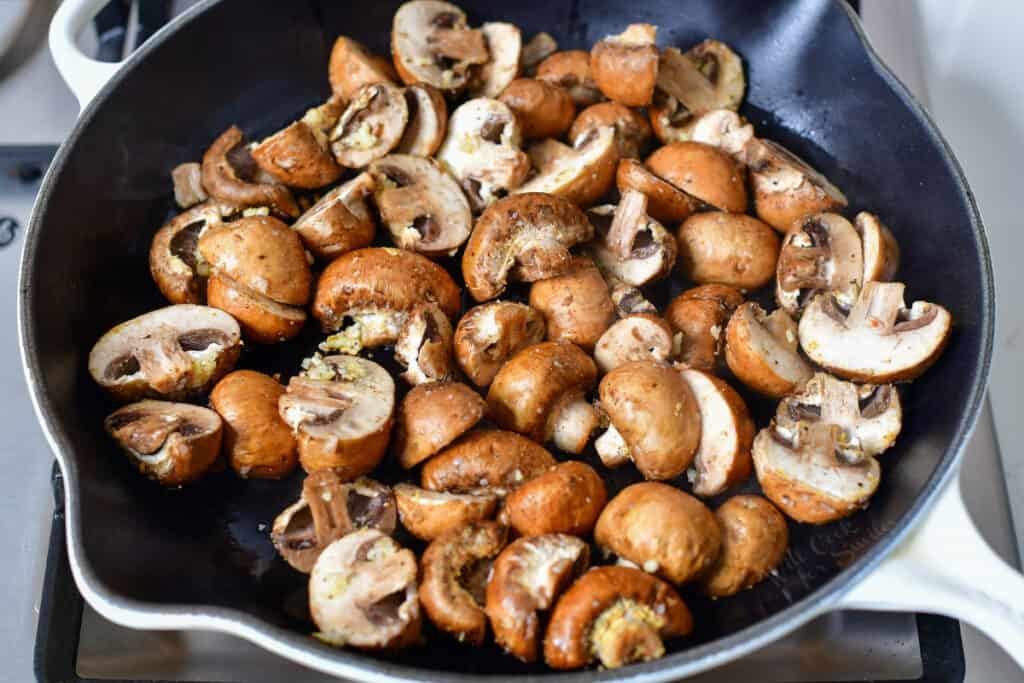 sauteeing sliced mushrooms in a skillet