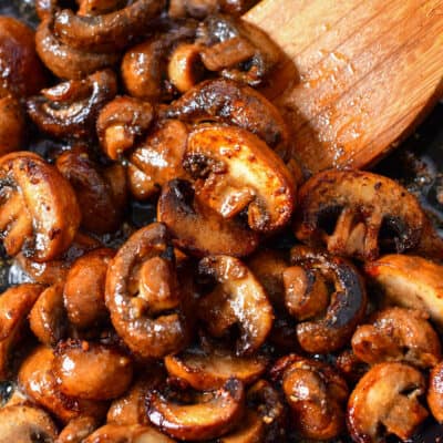 stirring sauteed mushrooms with wooden spoon in a skillet