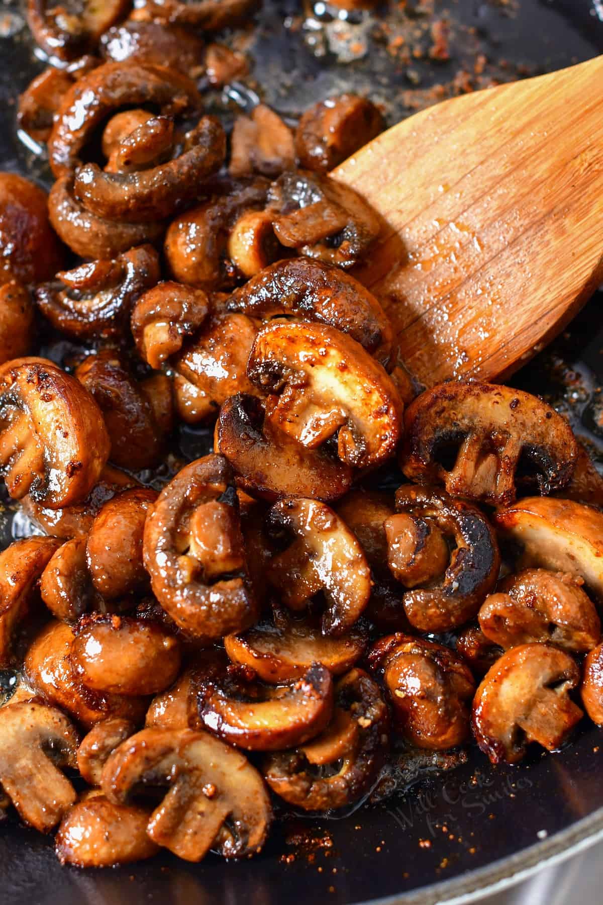 stirring sauteed mushrooms with wooden spoon in a skillet