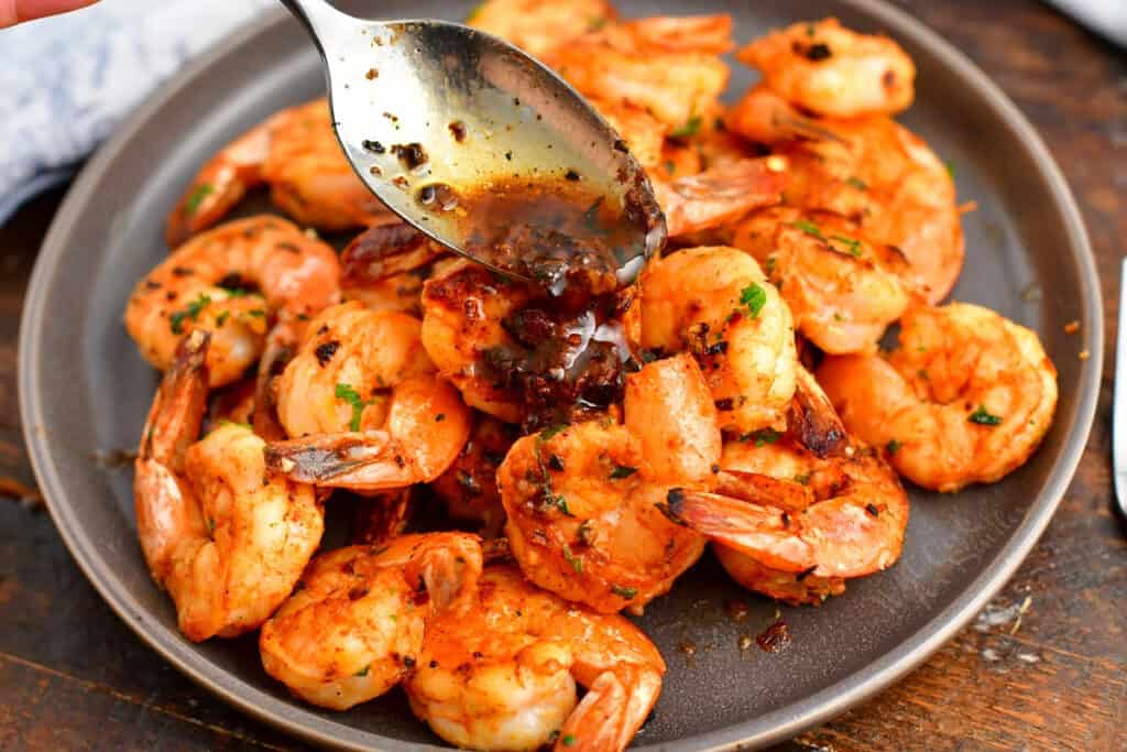 spooning garlic butter sauce over sautéed shrimp