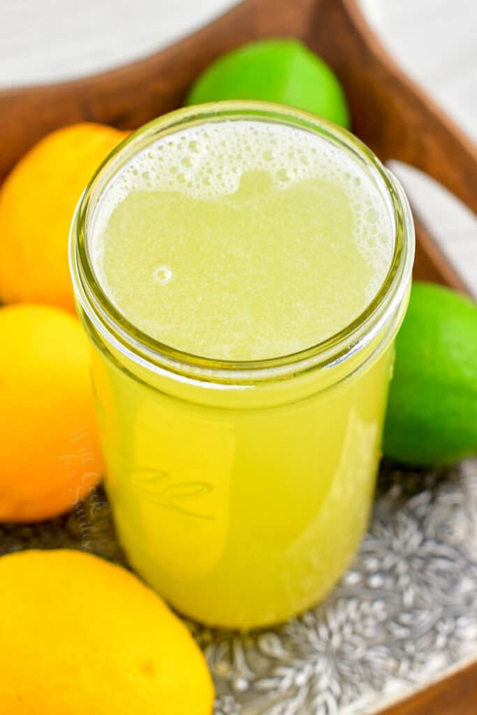 overhead: jar of citrus cocktail mixer and fresh fruit on a tray