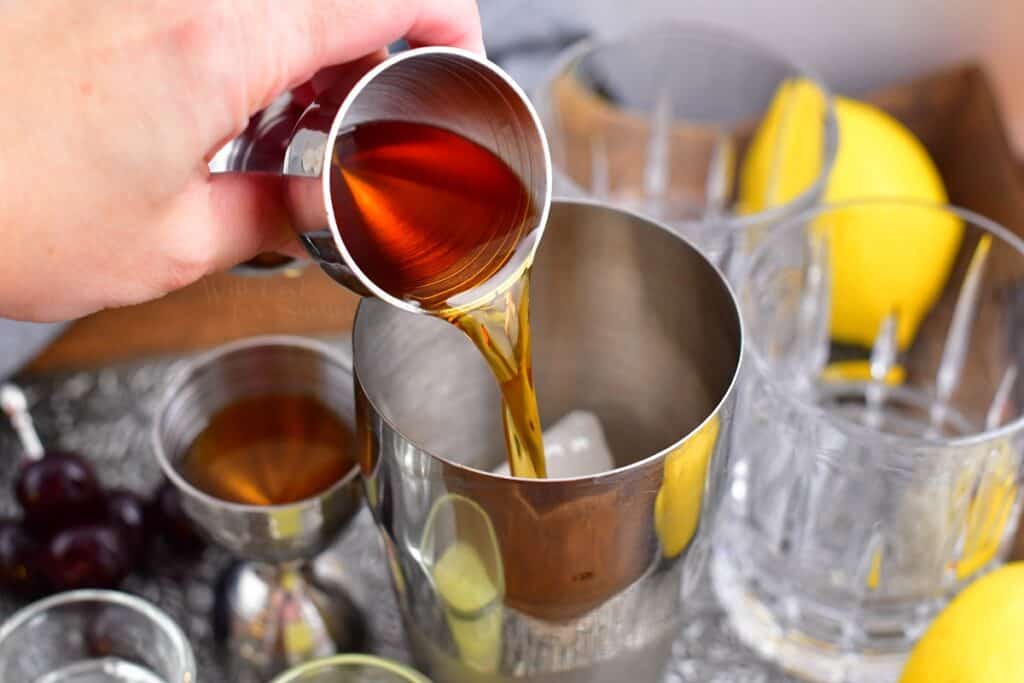 A dark liquor is being poured into a metal cocktail shaker.