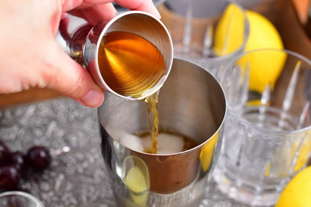 A lighter liquid is being poured into the cocktail shaker.