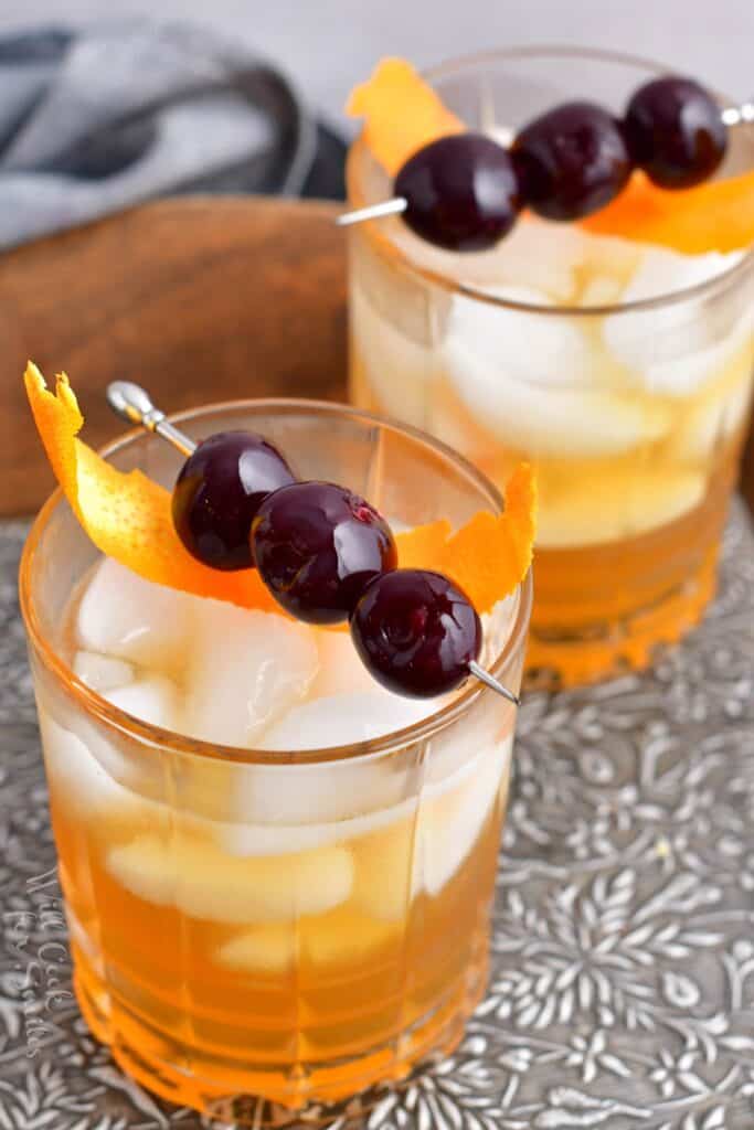 Two glasses filled with ice and amaretto sour cocktail are presented on a metal surface.