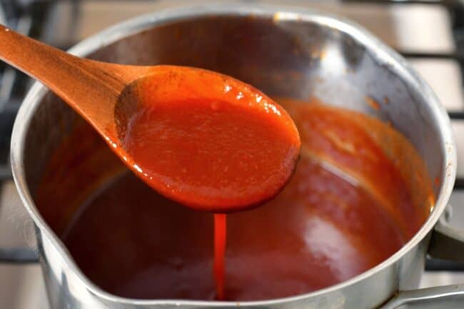 A wooden spoon is stirring the barbecue sauce in the pot.