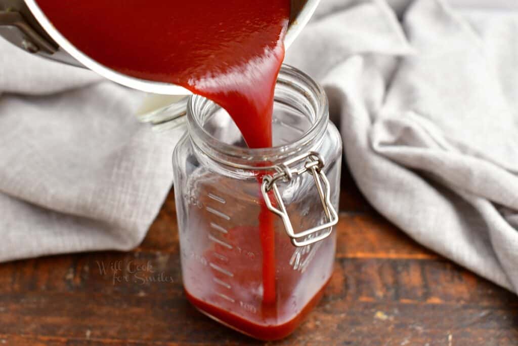 BBQ sauce is being poured into a mason jar.