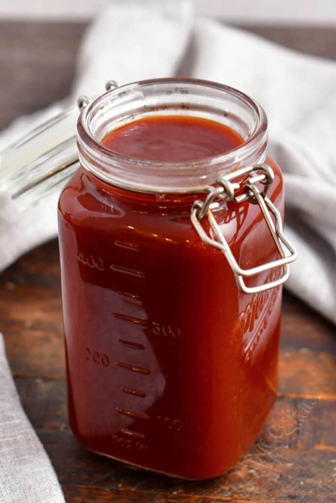 A jar of barbecue sauce is placed on a wooden surface. 