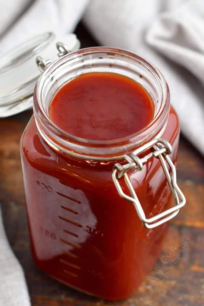 An open mason jar is filled with red BBQ sauce.