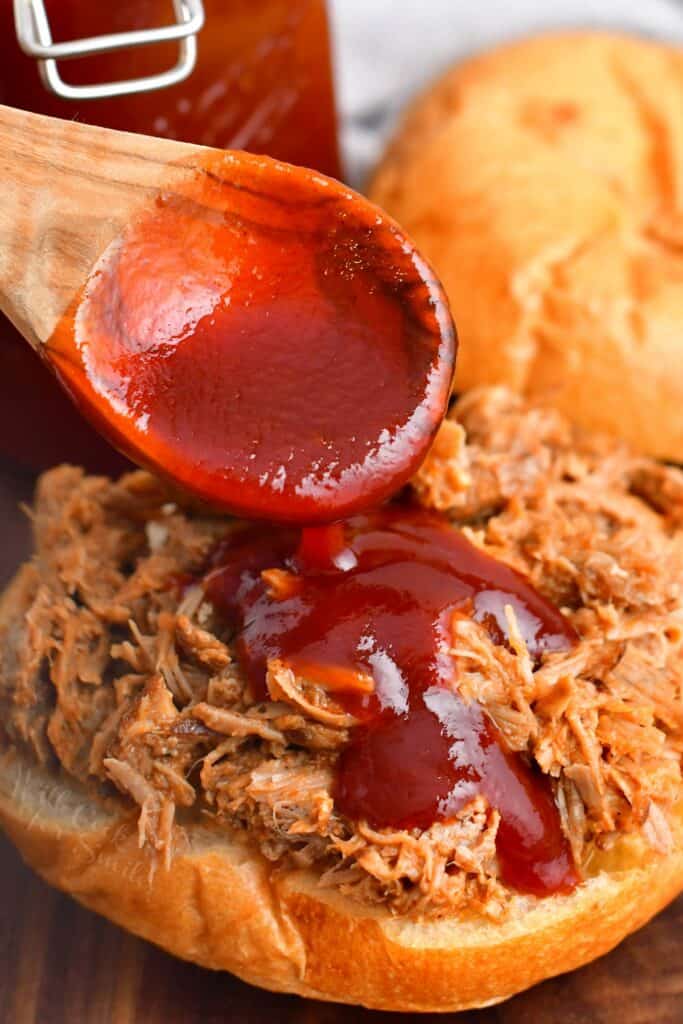 BBQ sauce is being drizzled onto a pulled pork sandwich. 