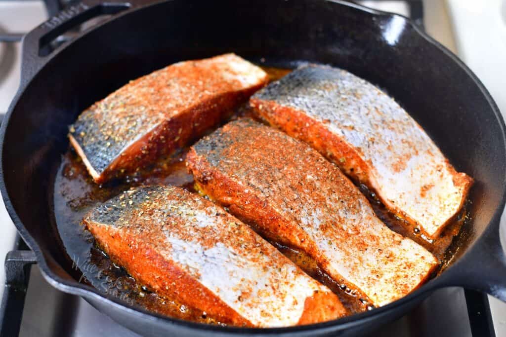 seasoned salmon fillets in a skillet on a stove