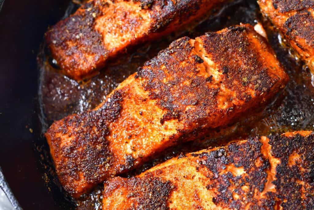 closeup of salmon seasoned and cooking in a skillet