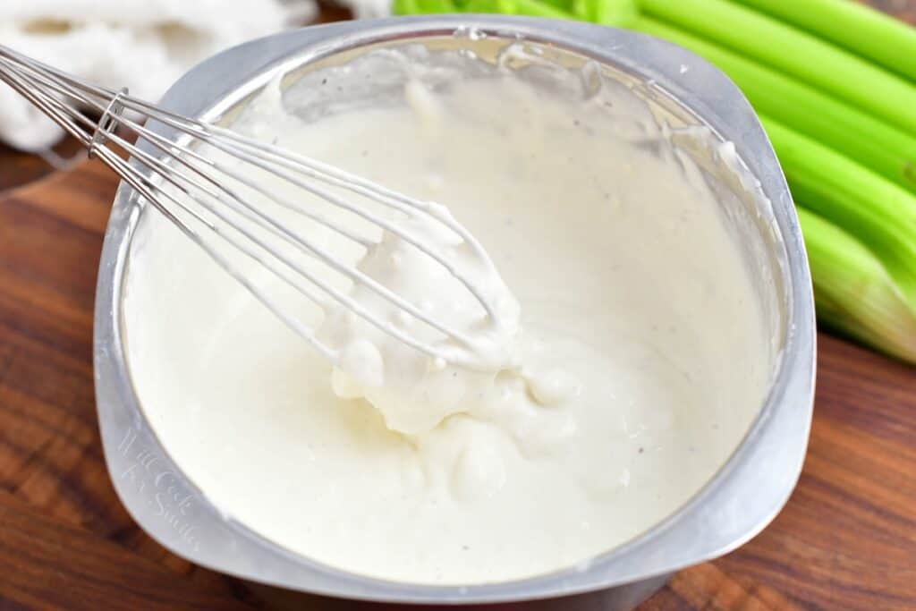 A whisk has combined all of the ingredients for blue cheese dressing.
