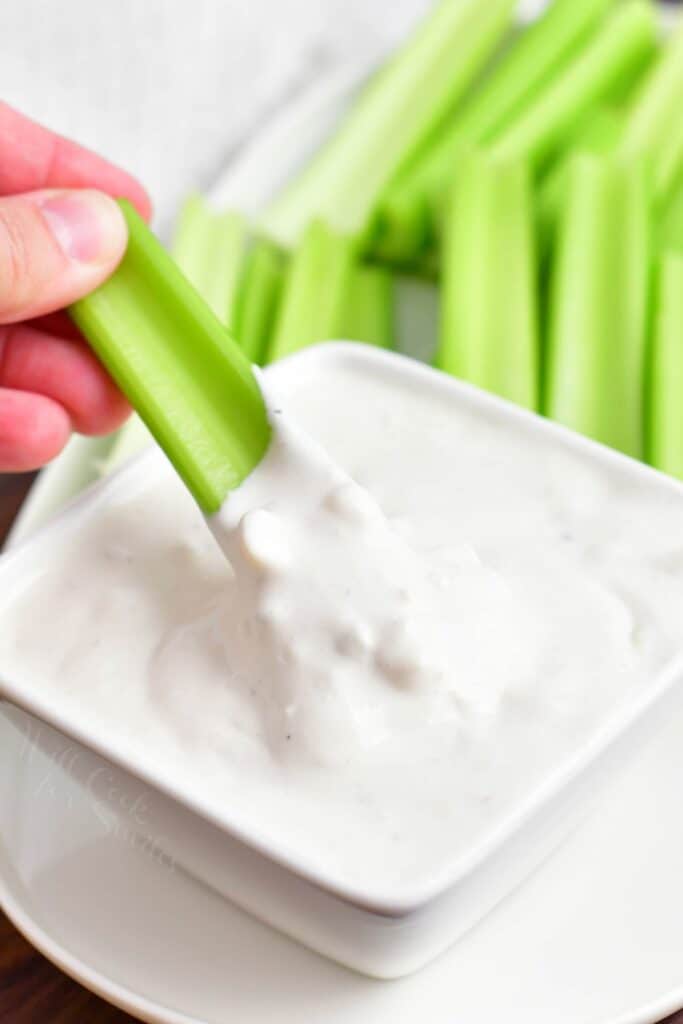 A piece of celery is dipped into a small bowl of blue cheese.