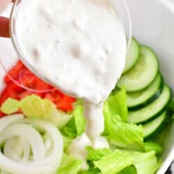 Blue cheese dressing is being poured on to a salad.