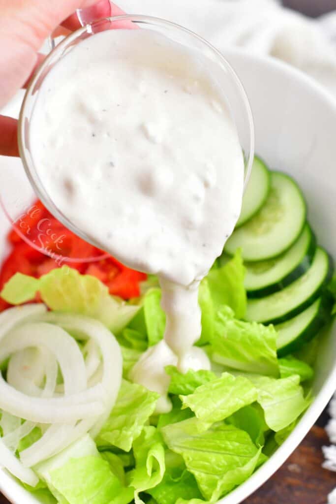 Blue cheese dressing is being poured on to a salad.