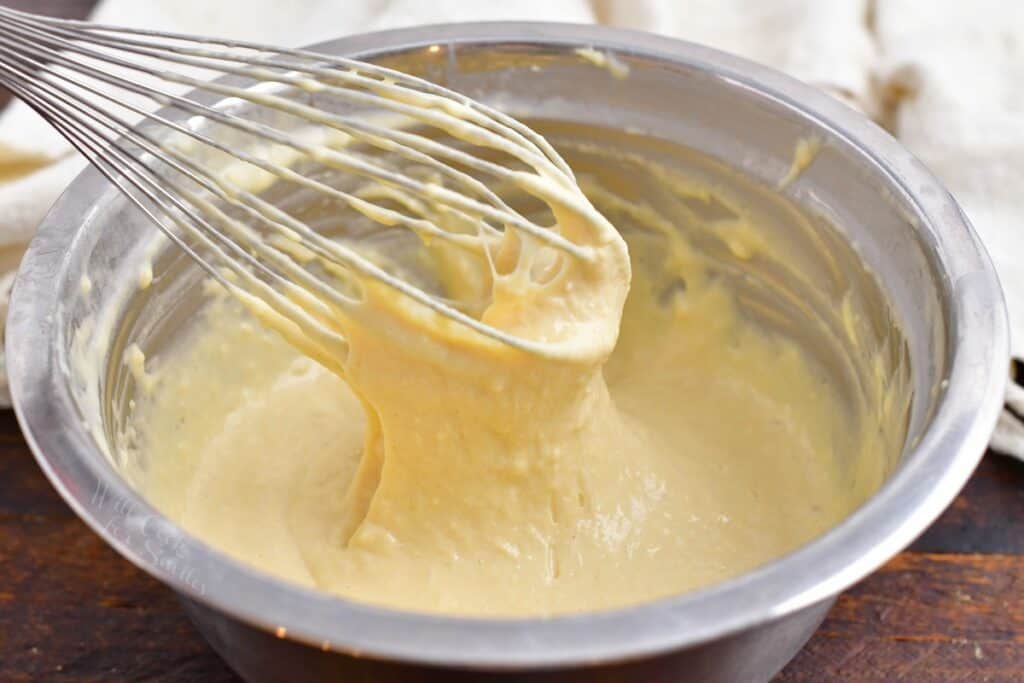 Pancake batter is being whisked in a large silver bowl. 