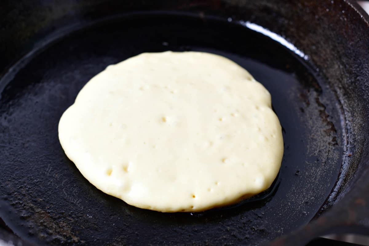 A pancake is on the griddle with bubbles in the batter, showing that it's ready to be flipped.